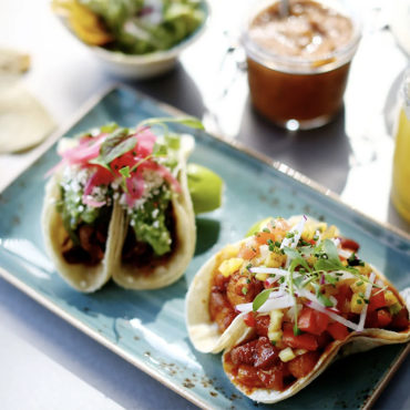 4 tacos garnished with fresh and pickled veggies on a turquoise plate.