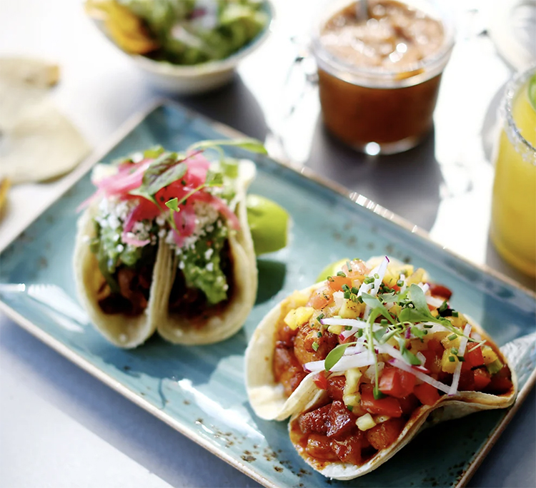 4 tacos garnished with fresh and pickled veggies on a turquoise plate.