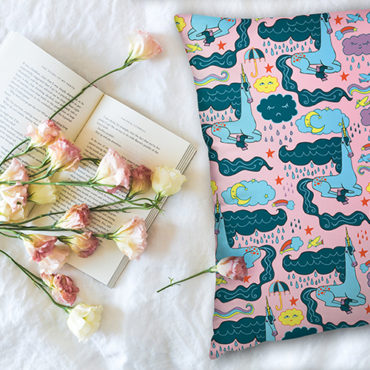 Rainy Day Unicorn Pattern on a Pink Pillow Laying Next to Pink and White Roses on top of a book