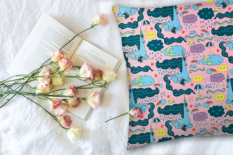 Rainy Day Unicorn Pattern on a Pink Pillow Laying Next to Pink and White Roses on top of a book
